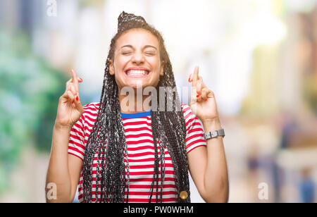 Junge geflochtenes Haar African American Girl über isolierte Hintergrund lächelnd die Daumen mit Hoffnung und die Augen geschlossen. Glück und abergläubischen Konzept. Stockfoto