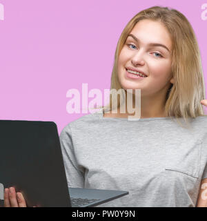 Junge kaukasier Frau mit Computer Laptop über isolierte Hintergrund mit einer Idee oder Frage Zeigefinger mit glücklichen Gesicht überrascht, Nummer eins Stockfoto