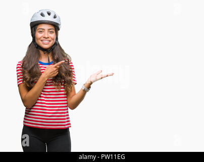 Junge arabische Radfahrer Frau tragen Schutzhelm über isolierte Hintergrund erstaunt und lächelt in die Kamera während der Präsentation mit Hand und zeigen Stockfoto