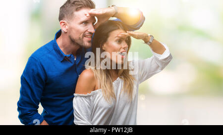 Junge Paare, die in Liebe über isolierte Hintergrund sehr glücklich und lächelnd weit entfernt, mit der Hand über den Kopf. Suche Konzept. Stockfoto