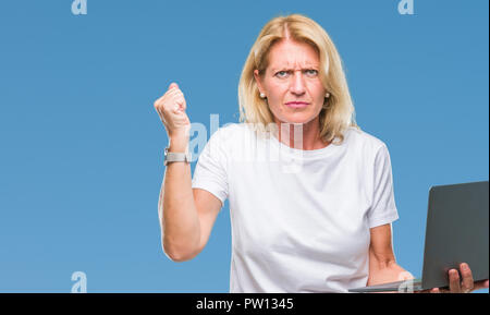 Mittleres Alter blonde Frau mit Computer Laptop über isolierte Hintergrund genervt und frustriert schrie mit Zorn, verrückt und schreien mit erhobener Hand, Stockfoto