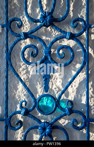 Detail der schmiedeeiserne Gitter mit dekorativen farbigen Glas auf einem rustikalen Stein Wand Stockfoto