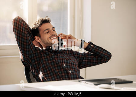 Unternehmer wieder entspannt auf seinem Stuhl und Gespräch am Handy an seinem Schreibtisch sitzen. Mann eine Pause von der Arbeit und Gespräch am Handy leanin Stockfoto