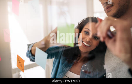 Business paar Schreiben auf Haftnotizen auf durchsichtigen Glaswand im Amt eingefügt. Büro Kollegen Diskussion von Ideen und Pläne auf einem TRANSPA Stockfoto