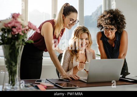 Gruppe von jungen Unternehmerinnen am Laptop suchen und lächelnd im Büro. Drei Kollegen zusammen arbeiten in moderner Arbeitsplatz. Stockfoto