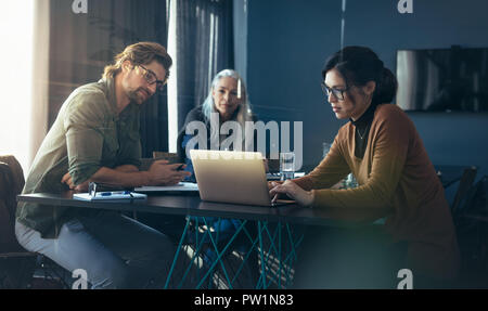 Drei Geschäftskollegen treffen sich in einem modernen Büro. Geschäftsfrau zeigt ihrem Team auf einem Laptop im Büro einen Geschäftsplan. Stockfoto
