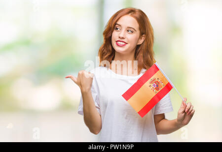 Junge schöne Frau mit Flagge von Spanien über isolierte Hintergrund zeigen und zeigt mit dem Daumen bis zu der Seite mit glücklichen Gesicht lächelnd Stockfoto