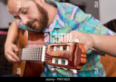 Bärtiger hippie Mann hand Einstellen der Akustik Gitarre. Close-up selektiven Fokus auf der Hand. Stockfoto