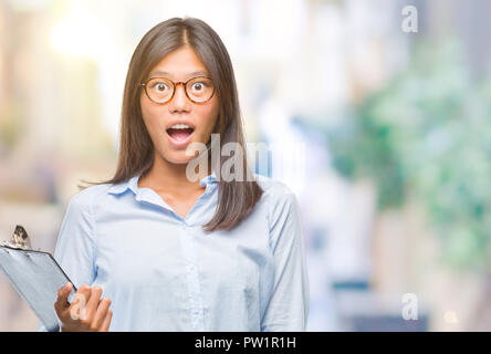 Junge asiatische Geschäft Frau über isolierte Hintergrund holding Zwischenablage Angst im Schlag mit einer Überraschung konfrontiert, ängstlich und aufgeregt mit Angst Ausdruck Stockfoto