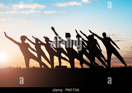 Silhouette von Menschen, die sich ausdehnende Übung gegen Himmel bei Sonnenuntergang Stockfoto