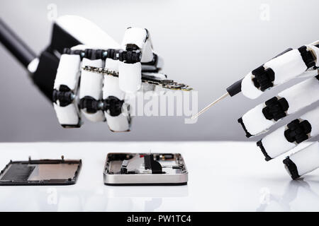 Nahaufnahme der Roboterhand Instandsetzung Smartphone mit einem Schraubendreher über Schreibtisch Stockfoto