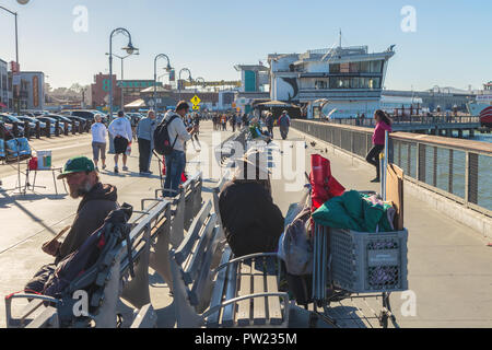 Zwei obdachlose Männer sitzen auf den Bänken am Fisherman's Wharf, mit Touristen im Hintergrund, San Francisco, Kalifornien, USA. Stockfoto