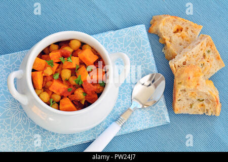 Hausgemachte kichererbse Kartoffel Curry in weiße Schüssel mit rustikalen Jalapeno cheddar Brot auf hellblauem Hintergrund. Horizontales format Schuß in natürlichen ligh Stockfoto