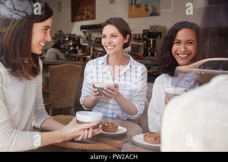 Weibliche Freunde reden im Coffeeshop, durch das Fenster gesehen Stockfoto