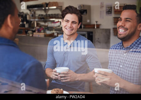Drei männliche Freunde lachen über Kaffee im Coffeeshop Stockfoto