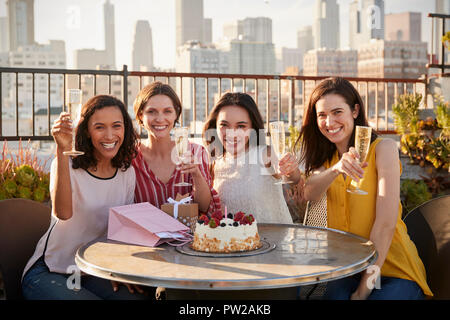 Portrait von weiblichen Freunde machen Toast zum Geburtstag feiern auf der Dachterrasse mit Sicht auf die City Skyline im Hintergrund Stockfoto