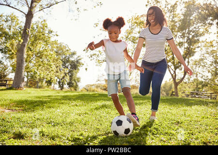Mutter und Tochter Fußball spielen im Park zusammen Stockfoto