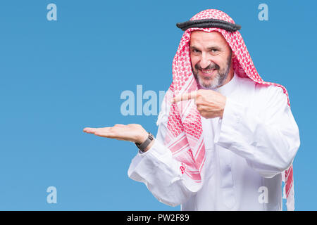 Senior arabischen Mann mit kufiya über isolierte Hintergrund erstaunt und lächelt in die Kamera während der Präsentation mit Hand und zeigte mit dem Finger. Stockfoto