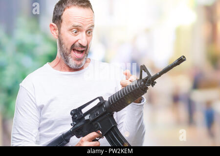 Mittleres Alter senior hoary kriminellen Mann mit Pistole Waffe über isolierte Hintergrund sehr glücklich zeigte mit Hand und Finger Stockfoto