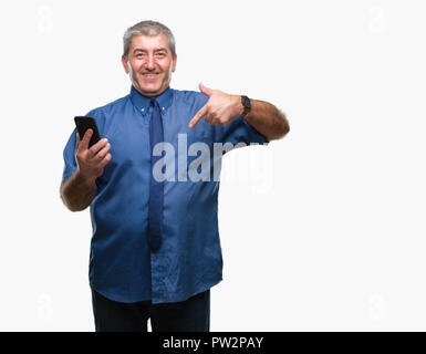 Gut aussehender älterer Mann sms senden Nachricht mit Smartphone über isolierte Hintergrund mit Überraschung Gesicht zeigenden Finger zu sich selbst Stockfoto
