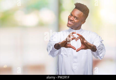 Junge arabische afrikanischen Mann mit traditionellen djellaba über isolierte Hintergrund in der Liebe mit Herz und mit Hand lächelnd. Romantische con Stockfoto