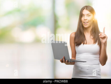 Junge Hispanic Frau mit Computer Laptop mit einer Idee oder Frage Zeigefinger mit glücklichen Gesicht überrascht, Nummer eins Stockfoto