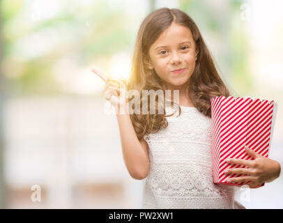 Brunette Hispanic Mädchen Popcorn essen sehr zufrieden zeigt mit Finger- und an der Seite Stockfoto