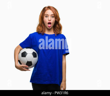 Junge schöne Frau über isolierte Hintergrund holding Fußball Fußball-ball Angst im Schlag mit einer Überraschung konfrontiert, ängstlich und aufgeregt mit Furcht Express Stockfoto