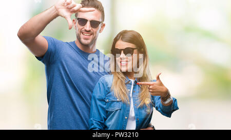 Junges Paar in Liebe Sonnenbrille tragen über isolierte Hintergrund lächelnd, Rahmen mit Händen und Fingern, glückliches Gesicht. Kreativität und photograp Stockfoto