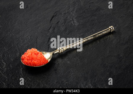 Ein Foto von roter Kaviar in einem Löffel auf einem schwarzen Hintergrund mit Kopie Raum Stockfoto