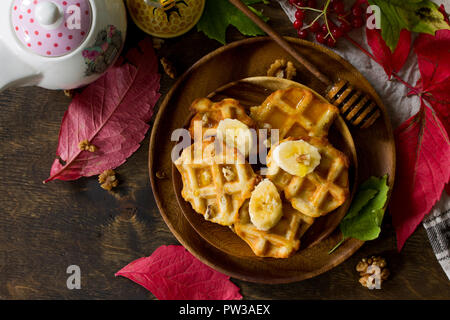 Thanksgiving backen. Belgische Nussbaum Wafer auf einer hölzernen Küchentisch, serviert mit frischem Bananenscheiben und Honig. Ansicht von oben flach Hintergrund. Kopieren Sie sp Stockfoto