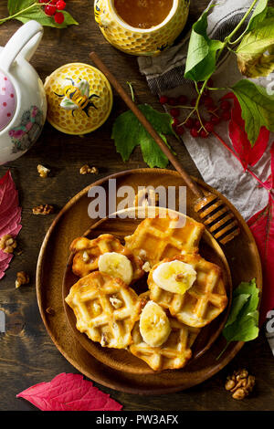 Thanksgiving backen. Belgische Nussbaum Wafer auf einer hölzernen Küchentisch, serviert mit frischem Bananenscheiben und Honig. Ansicht von oben flach Hintergrund. Stockfoto