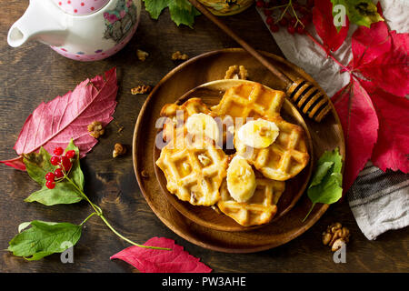 Thanksgiving backen. Belgische Nussbaum Wafer auf einer hölzernen Küchentisch, serviert mit frischem Bananenscheiben und Honig. Ansicht von oben flach Hintergrund. Stockfoto