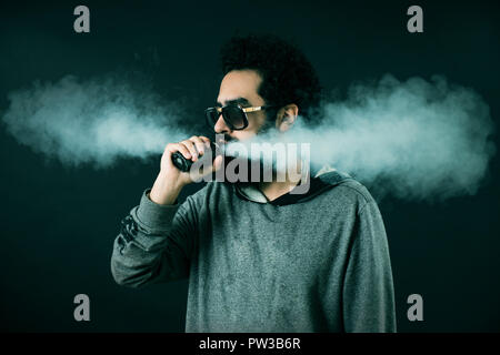 Vaping Mann hält ein Mod. Eine Wolke von Dampf. Schwarzen Hintergrund. Vaping eine elektronische Zigarette mit viel Rauch. Vape Konzept Stockfoto