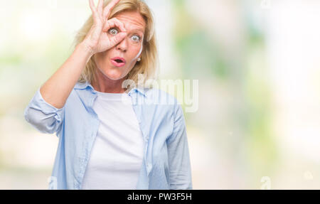 Blonde Frau mittleren Alters über isolierte Hintergrund tun ok Geste mit Gesicht überrascht, schockiert, Auge durch die Finger schauen. Die ungläubigen Ausdruck. Stockfoto
