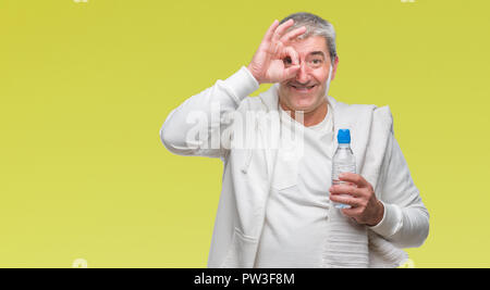 Gut aussehender älterer Mann Ausbildung, Handtuch und Trinkflasche über isolierte Hintergrund mit glücklichen Gesicht lächelnd tun ok Zeichen mit der Hand im Auge. Stockfoto