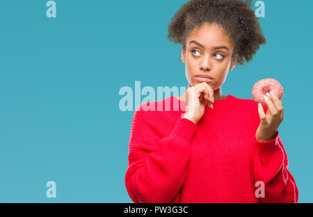 Junge afro-amerikanische Frau essen Donut über isolierte Hintergrund ernstes Gesicht denken über Frage, sehr verworrene Vorstellung Stockfoto