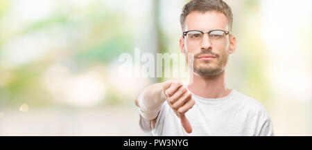 Junge tätowiert erwachsenen Mann suchen unzufrieden und wütend, Ablehnung und negativ mit Daumen nach unten Geste. Schlechter Ausdruck. Stockfoto