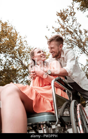 Positiver Mann lachend während umarmte Geliebte behinderte Frau Stockfoto