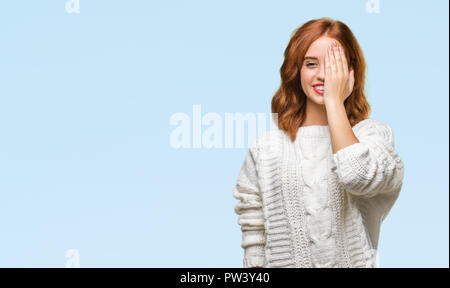 Junge schöne Frau über isolierte Hintergrund tragen Winter pullover Abdecken eines Auges mit der Hand mit selbstbewussten Lächeln auf dem Gesicht und Überraschung Emotion. Stockfoto