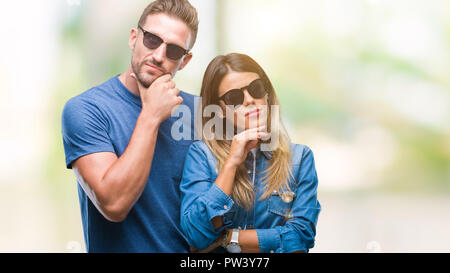 Junges Paar in der Liebe tragen Sonnenbrillen über isolierte Hintergrund mit der Hand am Kinn über die Frage denken, nachdenklichen Ausdruck. Lächelnd mit thoughtfu Stockfoto