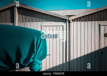 Details von den schönen weißen Strand Hütten in Europa. Windig, sonnigen Tag, blau Schal im Vordergrund, Fertighaus minimalistisch Unterstände im Hintergrund. Ruhiger Stockfoto