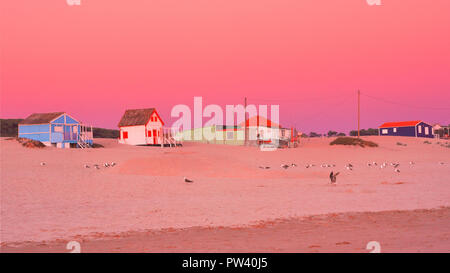 Bunten Strandhäuser an der Costa da Caparica in Lissabon am Strand, bei Sonnenuntergang mit einem orangefarbenen Himmel und goldenen Sandstrand anzeigen Stockfoto