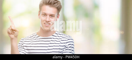 Jungen gutaussehenden blonden Mann Streifen tragen Sailor t-shirt Sehr zufrieden zeigt mit Finger- und an der Seite Stockfoto