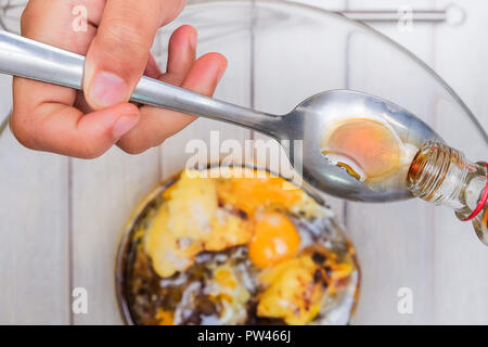 Eine Asiatische jugendlich Junge gießt ein Teelöffel Vanille in die Schüssel für die berühmte amous extrahieren. Essen und Kochen. Stockfoto