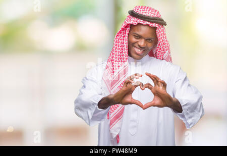 Junge arabische afrikanischen Mann mit traditionellen Kufiya über isolierte Hintergrund in der Liebe mit Herz und mit Hand lächelnd. Romantische con Stockfoto