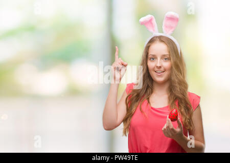 Junge blonde Frau bekleidet Osterhasen Ohren mit einer Idee oder Frage Zeigefinger mit glücklichen Gesicht überrascht, Nummer eins Stockfoto