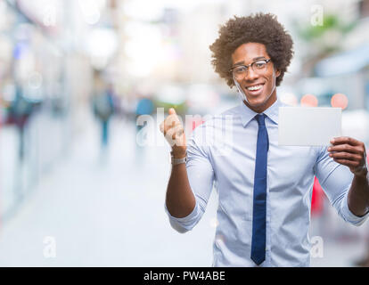 Afro-amerikanische Mann hält eine leere Karte über isolierte Hintergrund schreien stolz und feiern Sieg und Erfolg sehr aufgeregt, jubelnde Emotion Stockfoto