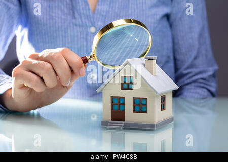 Nahaufnahme einer Hand, die Lupe ist eine Geschäftsfrau Glas über Haus Modell über Schreibtisch Stockfoto