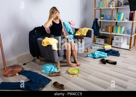 Verärgert Frau sitzt auf einem Sofa durch Scatted Kleidung Umgeben Stockfoto